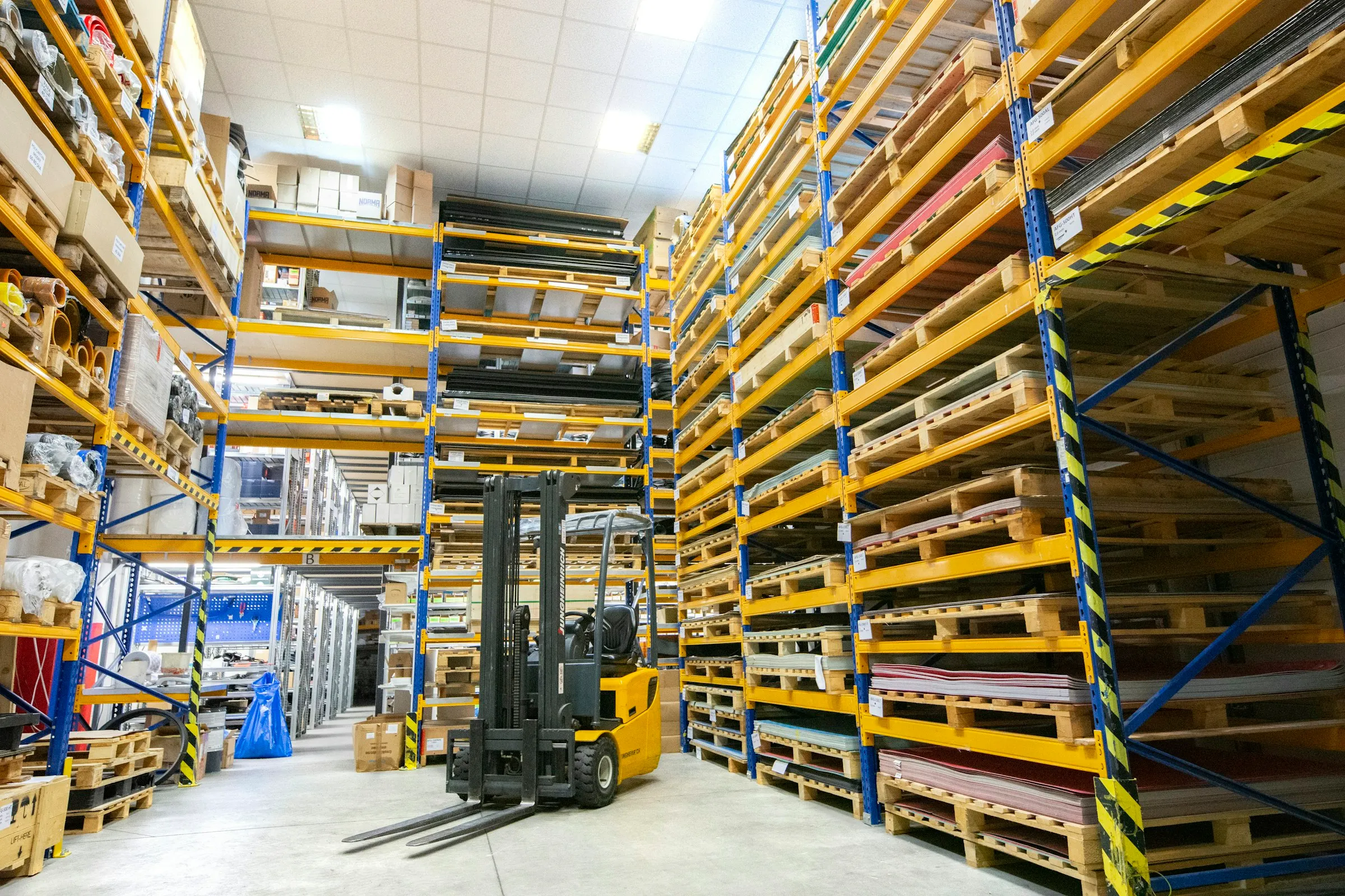 Yüksek raflı bir depoda paletler, koliler ve forklift (temsili görsel)